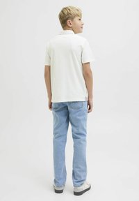 Polo blanc à manches courtes, associé à un jeans en denim bleu clair. L'arrière présente un col et une couture détaillée au niveau de l'ourlet.