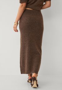 Brede bruine maxi-rok van zacht materiaal, met een aansluitende taille en een zijsplit, gecombineerd met hoge bruine schoenen. Eenvoudig ontwerp en elegante textuur.