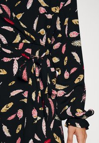 Černé šaty z látky s vzory v podobě růžových, červených a béžových peříček, s opaskem na zavázání v pase a dlouhými nafouknutými rukávy s volánkovými manžetami.