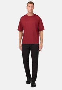 T-shirt rossa a maniche corte con una vestibilità rilassata, abbinata a pantaloni neri. La maglietta presenta un colletto rotondo e una texture di tessuto liscia.