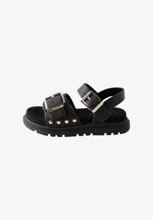 Schwarze Sandalen mit zwei verstellbaren Schnallen, goldenen Hardware-Akzenten, strukturiertem schwarzen Fußbett und einer dicken schwarzen Gummisohle mit Profil.