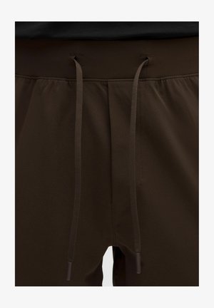 Elastische tailleband met lange bruine trekkoorden aan donkerbruine zachte stoffen broek of korte broek, met zichtbare stiksels en geplooid materiaal.