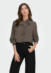 Blusa marrone con motivo, collo con fiocco, maniche lunghe, polsini elastici e dettagli in contrasto blu scuro su collo e polsini.