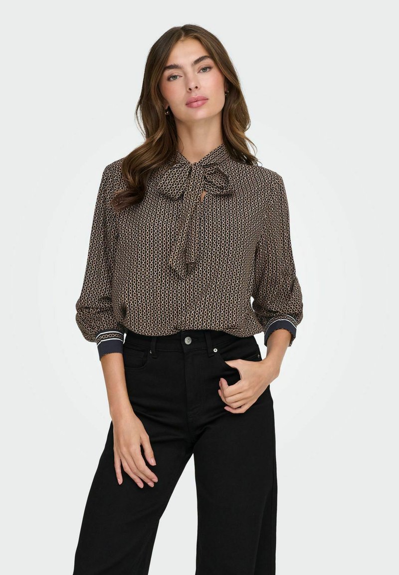 Blusa marrone con motivo, collo con fiocco, maniche lunghe, polsini elastici e dettagli in contrasto blu scuro su collo e polsini.