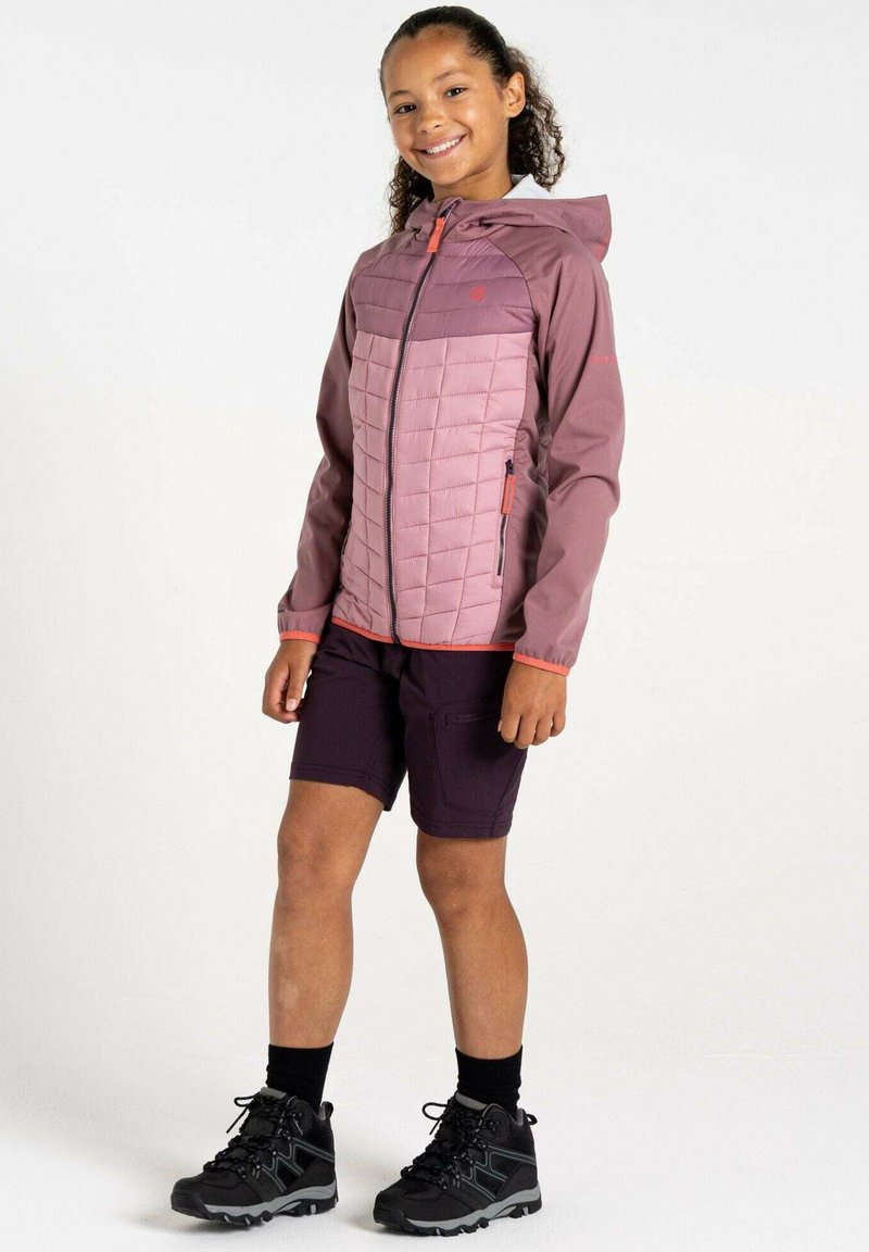 Hellpurpuroe isolierte Jacke mit Kapuze, gestepptem Design, kontrastierenden Ärmeln, kombiniert mit dunklen Shorts und schwarzen Wanderschuhen.