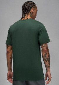 Camiseta de manga corta de color verde oscuro con cuello redondo, fabricada en algodón, de textura suave y con un diseño de espalda sin adornos.