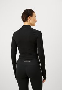 Svart långärmad träningströja med hög krage och kroppsnära design, tillverkad av mjukt material, kombinerat med svarta träningstights.