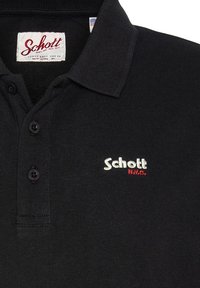 Sort polo-shirt lavet af tekstureret bomuld, med krave og tre sorte knapper. "Schott"-logo i broderet hvidt og rødt på brystet.