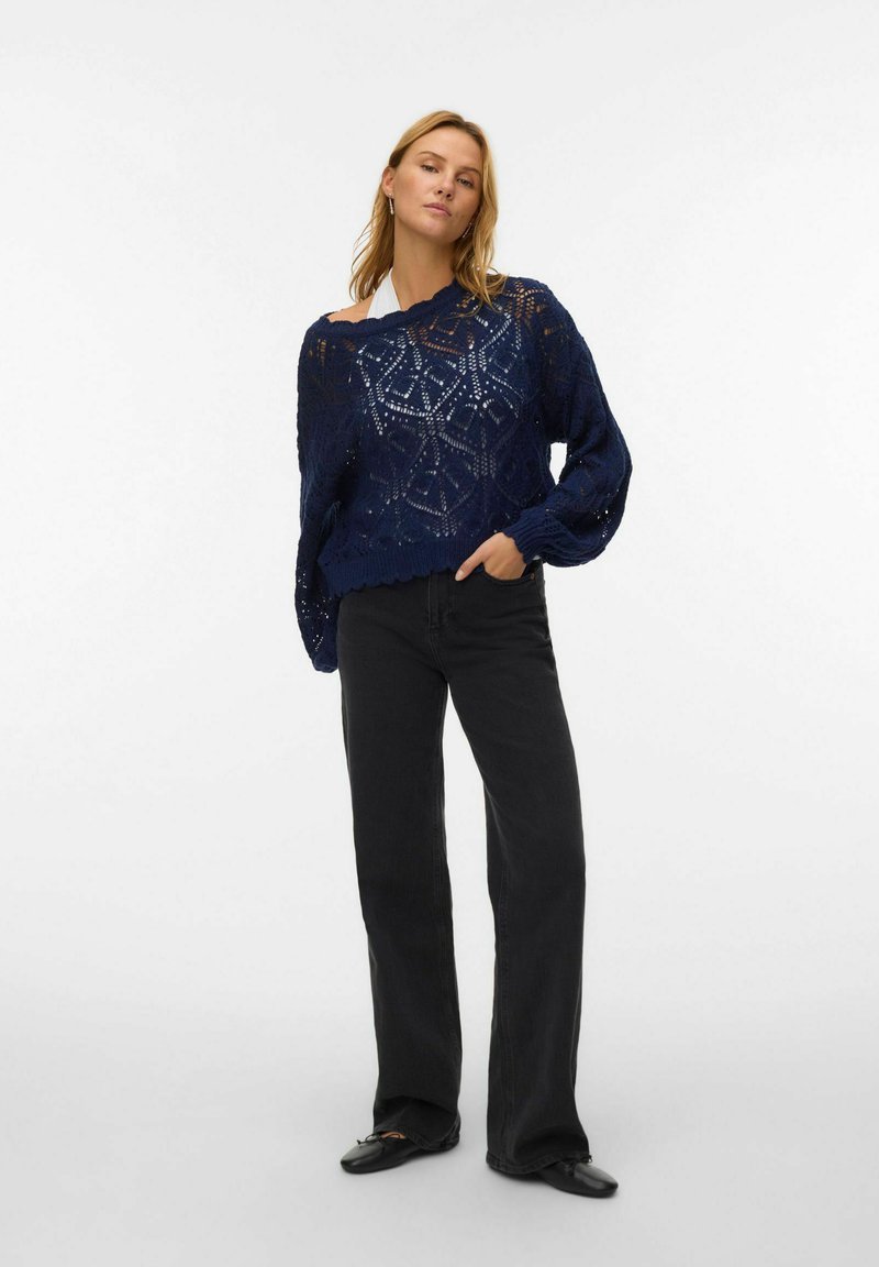 Maglione lavorato a maglia blu navy con un design morbido, caratterizzato da un motivo traforato e maniche larghe, abbinato a pantaloni neri a vita alta.