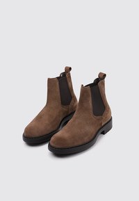 Botas Chelsea de ante marrón con paneles laterales elásticos, punteras redondeadas y suelas de goma negra con detalles de costura.