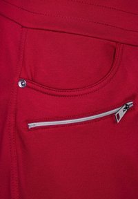 Rode stof met een gladde textuur heeft een voorkantzak met een zilveren ritssluiting en een decoratieve zilveren knoopaccent.