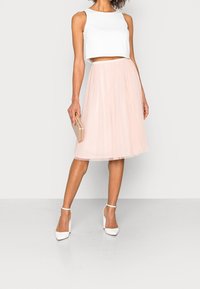 Un top court blanc associé à une jupe en tulle rose, des chaussures à bride de cheville blanches et un sac à main doré. Tissu lisse et texture superposée.