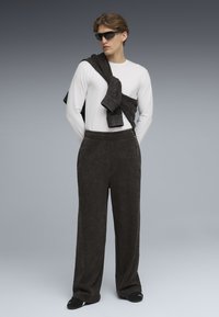 Sorte, strukturerede sweatpants med elastisk talje, parret med en hvid langærmet skjorte og en mørk sweater draperet over skulderen.