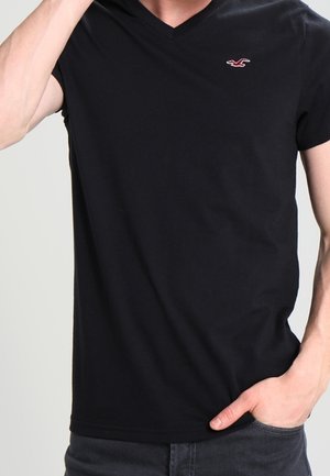 Black V-neck T-shirt made of cotton, featuring short sleeves and a small red logo on the left chest. Smooth texture, fitted design.