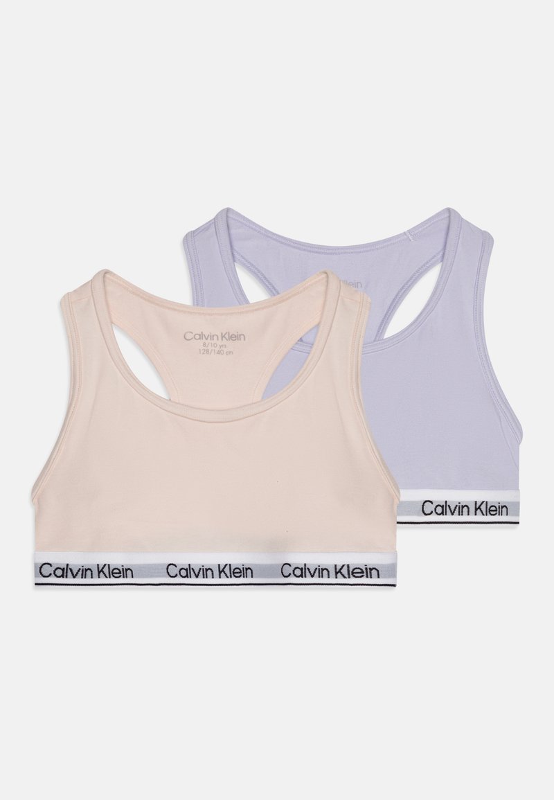 Δύο σουτιέν γυμναστικής, ένα κρέμα και ένα ανοιχτό μοβ, με ομαλή υφή και φαρδιές ραμμένες τιράντες. Και τα δύο διαθέτουν ελαστική ζώνη με λογότυπο.