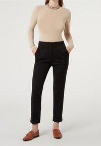 Långärmad beige topp kombinerad med svarta skräddarsydda byxor med knappstängning och sidofickor, kompletterat med bruna loafers.