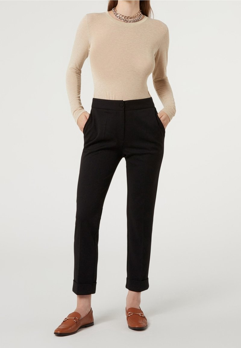 Långärmad beige topp kombinerad med svarta skräddarsydda byxor med knappstängning och sidofickor, kompletterat med bruna loafers.