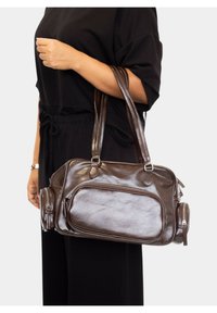 Bolso de mano de cuero marrón con dos asas, bolsillo frontal con cremallera, textura suave, bordes redondeados y compartimentos laterales para almacenamiento.