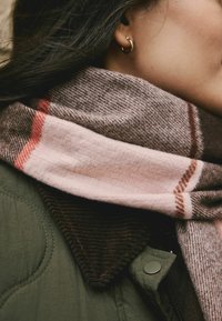 Brown and pink plaid scarf made of soft fabric, wrapped around a collar of a dark green jacket with a textured brown corduroy section.
