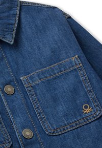 Jeansowa kurtka w ciemnoniebieskim kolorze z zapinanym kołnierzem, dwoma przednimi kieszeniami i kontrastowym, żółtym przeszyciem. Posiada małe logo na kieszeni.