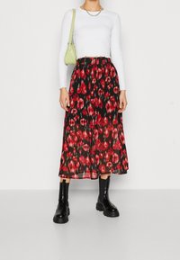 Gonna nera a fiori con motivi rossi e rosa, tessuto leggero, lunghezza media, abbinata a un top bianco corto a maniche lunghe e stivali neri.