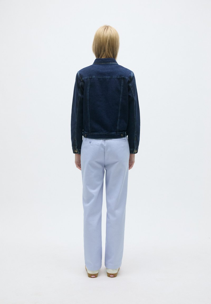 Donkerblauwe denimjas met een rechte pasvorm, gekenmerkt door een knoopsluiting en zijzakken, gecombineerd met lichtblauwe recht-toe-rechtaan broek.