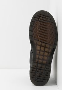 Suola di scarpa nera in gomma texturizzata, con un grip a motivo e marchi del brand visibili. Forma curvata e senza dettagli sporgenti.