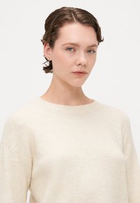 Beżowy sweter z okrągłym dekoltem i opuszczonymi ramionami. Miękka tekstura i lekki materiał. Prosty design, bez wzorów ani akcentów.