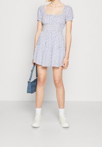 Bílé šaty s malým modrým květinovým vzorem, upnutý korzet, krátké nabírané rukávy a široká sukně. Připárovány s džínsovou taškou a bílými teniskami.