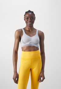 Lys grå sports-bh med ribbet tekstur, justerbare stropper og mesh-detaljer, kombinert med høyt liv-gule tights.
