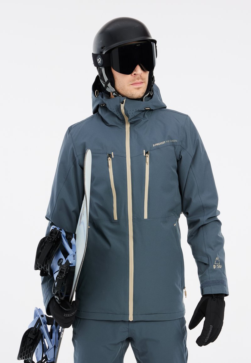 Skijacke in Dunkelblau mit beigen Reißverschlüssen, Kapuze und Belüftungslöchern; kombiniert mit einem schwarzen Helm, Skibrille und Snowboardbindungen.