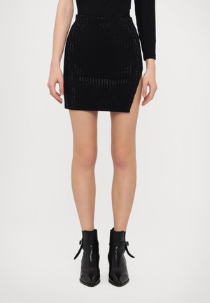 Black sequined mini skirt with vertical ribbed texture and a side slit. Worn with black ankle boots featuring buckle accents.