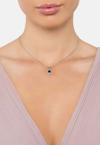Collana in argento con pendente rettangolare di pietra blu circondato da piccole pietre chiare, adagiata su un collo liscio.