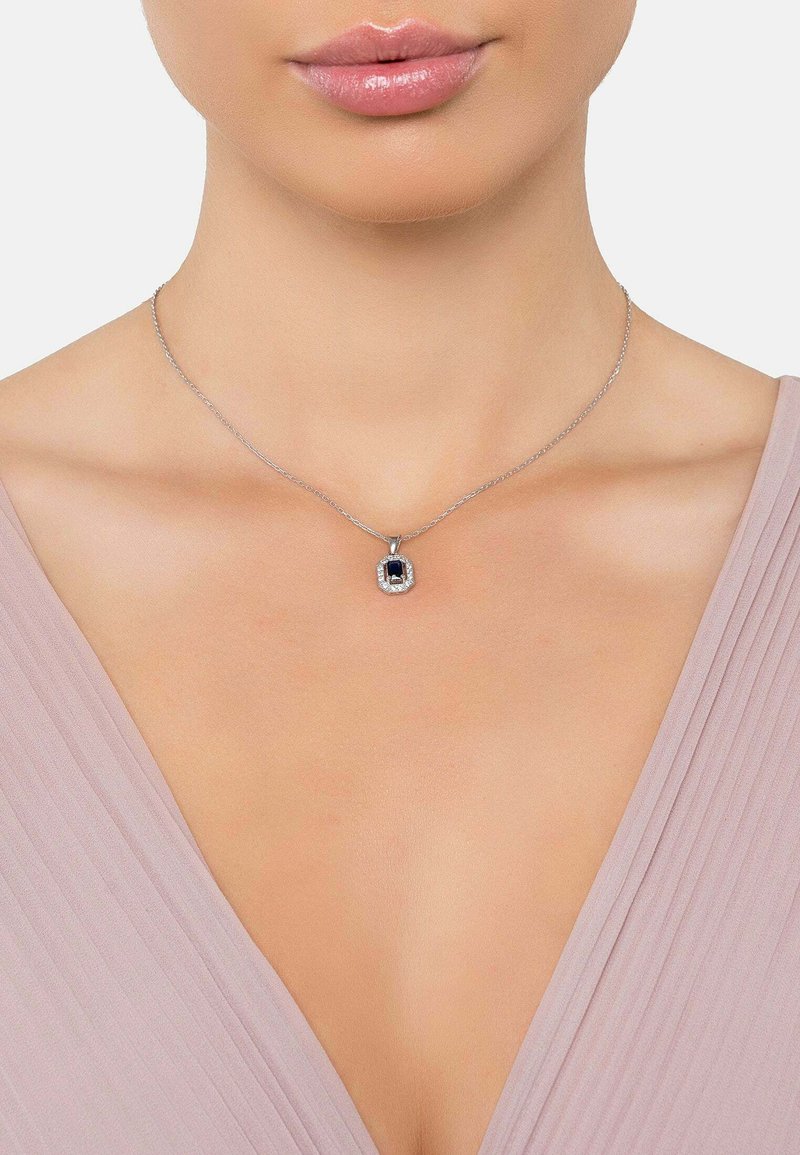 Collana in argento con pendente rettangolare di pietra blu circondato da piccole pietre chiare, adagiata su un collo liscio.