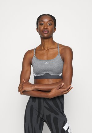 Grå idretts-BH med justerbare tynne stropper, med et lyst grått panel og svart akksent, kombinert med mønstrede svarte leggins.