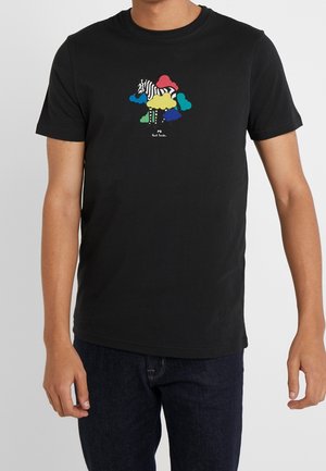 Homme portant un t-shirt noir avec un motif coloré de zèbre et de nuage centré sur la poitrine et un jean bleu foncé.