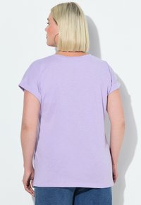 Camiseta de manga corta color lavanda con mangas enrolladas, escote redondo y textura suave. Detalle de costura visible en el dobladillo y el escote.