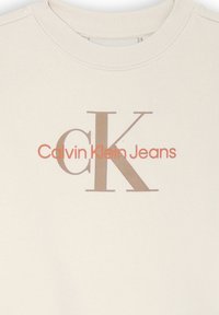 Felpa beige con scollatura a coste che presenta il testo "Calvin Klein Jeans" in arancione e marrone. Tessuto morbido e con texture.