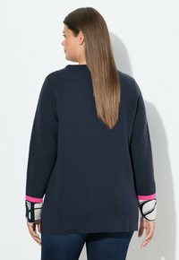 Dunkelblauer Pullover mit langen Ärmeln, der rosa und gemusterte Akzente an den Bündchen aufweist, aus weichem, strukturiertem Stoff gefertigt.