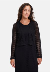 Schwarze Strickjacke mit offenem Vorderteil und langen Ärmeln, die ein strukturiertes Muster aufweist und locker sitzt. Der Stoff ist leicht und atmungsaktiv.