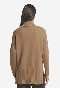 Hellbrauner Rollkragensweater aus weichem Strick. Mit geripptem Saum und seitlichen Schlitzen. Lässige Passform mit überschnittenen Schultern, minimalistisches Design.