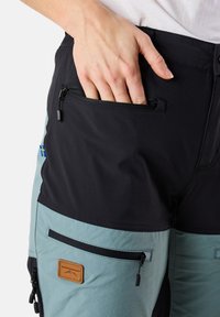 Moniväriset shortsit, joissa on musta ja vaaleansininen design, vetoketjulliset taskut, tekstiilipatchit ja sileä rakenne.