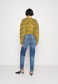 Suéter a rayas amarillas y negras, jeans azules y mules negros de tacón. El suéter tiene un corte holgado; los jeans son ajustados con bolsillos traseros.