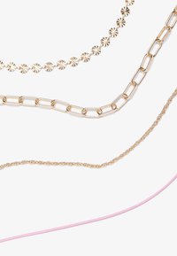 Fyra halsband arrangerade horisontellt: en guldstjärnformad design, en länkad kedja, en vriden guld kedja och en tunn rosa snöre.