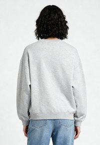 Felpa grigia con vestibilità rilassata, spalle a caduta, polsini e orlo a coste. Tessuto morbido, senza loghi o motivi visibili sul retro.