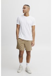 White cotton t-shirt, beige textured shorts, and light sneakers. The outfit features a relaxed fit, with the shorts having a slight pattern.