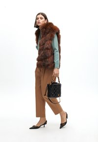 Hnědá kožušinová vesta přes tyrkysový svetr, béžové kalhoty a černé lodičky. Vzhled doplňuje texturovaná černá kabelka s řetízkovým popruhem.