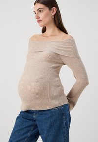 Beige ribbed knit off-the-shoulder sweater with long sleeves, form-fitting design, and soft texture, paired with blue denim jeans.