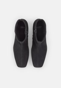 Bottes noires en daim à chevilles avec une texture lisse, une forme angulaire et des zips latéraux. Présentent un design minimaliste sans embellissements visibles.