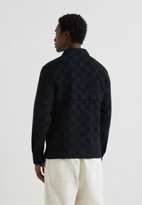 Giacca a camicia a motivi quadrettati nera con un tessuto testurizzato, maniche lunghe e polsini con bottoni, caratterizzata da un dettaglio a yoke sul retro.